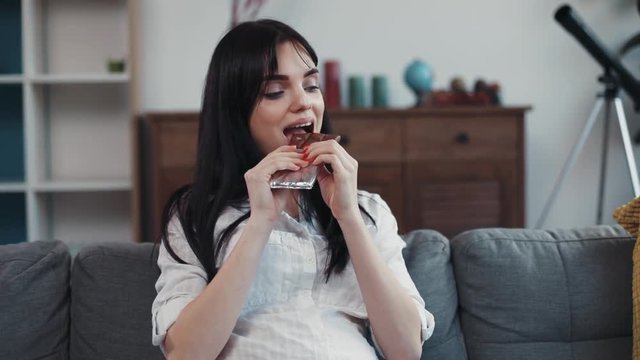 Portrait pregnant woman resting on sofa eating chocolate touching her pregnant belly home baby nutrition love child food girl house beautiful happy sweet healthy brunette young attractive smile