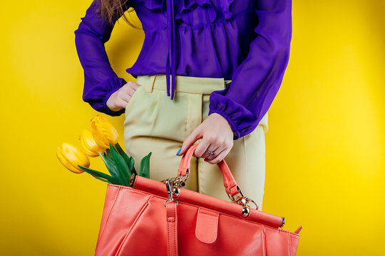 Studio shot of a young woman wearing spring outfit and holding a bag with yellow tulips