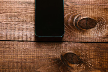 Top view of a modern smartphone with large screen on vintage wooden table. Blank empty display