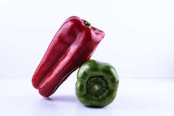red and green pepper, where the red is placed on top of the green on a white background