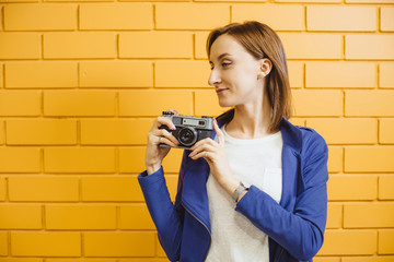 Beautiful crazy girl with retro metal film camera on background yellow brick wall.