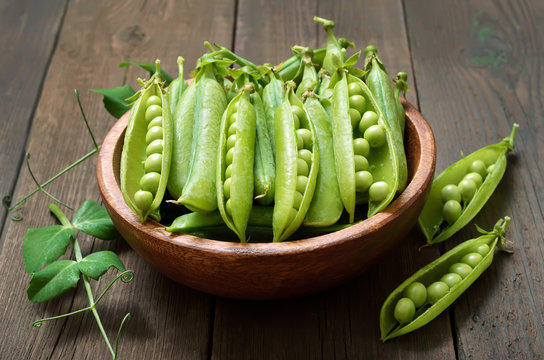 Pods of green peas in wooden bowl