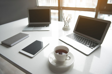 Fototapeta premium Cup of tea near digital device, laptop and copybook locating on desk in room. Design concept