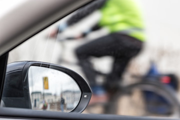 Part inside view of a car, a car mirror and a partial view of a cyclist