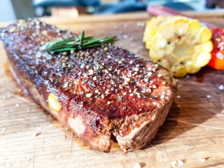 Beef steak sprinkled with pepper and salt lies on a Board with corn and tomatoes.
