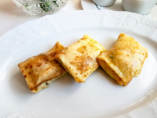 Pancakes with flesh rolled envelope lie on a white plate.