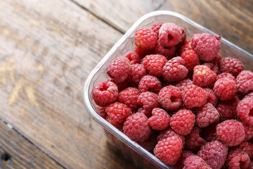 fresh raspberries in a plastic container on a wooden background