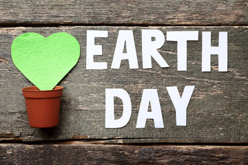 Inscription Earth Day with green heart and pot on grey wooden table