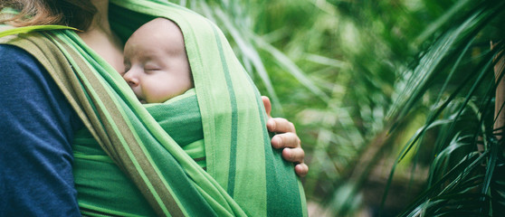 A young mother with a baby in a sling is walking in the jungle