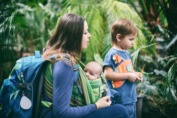 A young mother with a baby in a sling and little boy is walking in the jungle