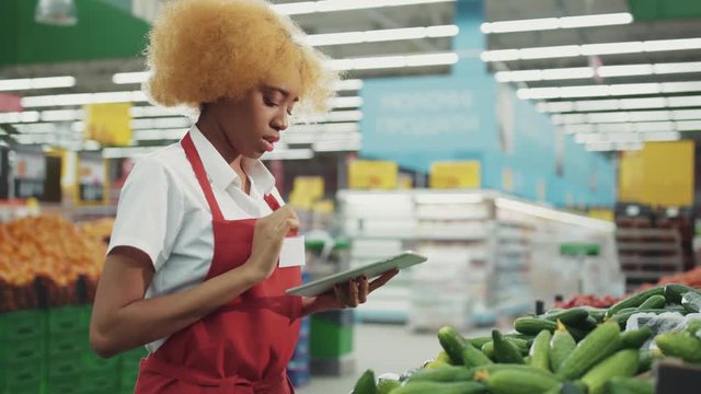 Beautiful african american woman seller uses tablet to work in the vegetable department light at supermarket black industry worker grocery market healthy staff produce job service retail store shop
