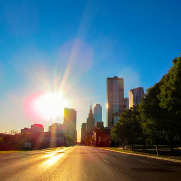 Street Cityscape At Sunset In Downtown Of Dallas, Texas, USA.
City Skyline With Modern Buildings And Skyscrapers In City Center District Against A Bright Sun. View From Empty Road.