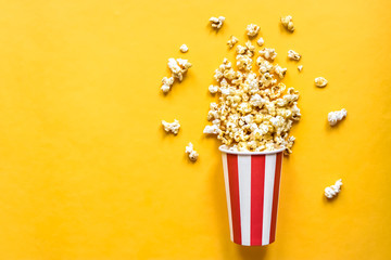 Popcorn in a red and white cardboard box on a yellow background.  - obrazy, fototapety, plakaty