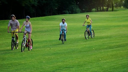 Four cheerful students cycling on green lawn. Group of young bikers cycling through park. Happy summe holiday.