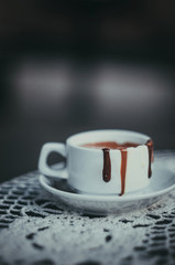 A cup of hot chocolate on a plate with leaking dark, milk and white chocolate. Vertical shot