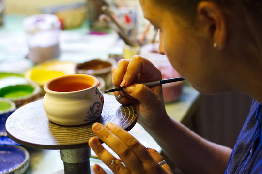 Woman working In her pottery studio. Ceramic workshop. Paint on clay cup in the pottery. 