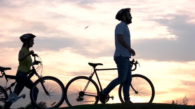 Young couple walking at sunset. Young man and woman with bicycles at sunset. Amazing rest together outdoors.