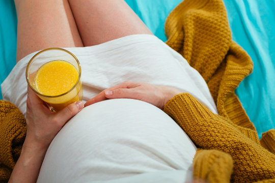 Pregnant woman drinking orange juice. Aerial close up view.