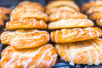 Macro closeup display of white covered drizzled danish pastries in bakery for breakfast