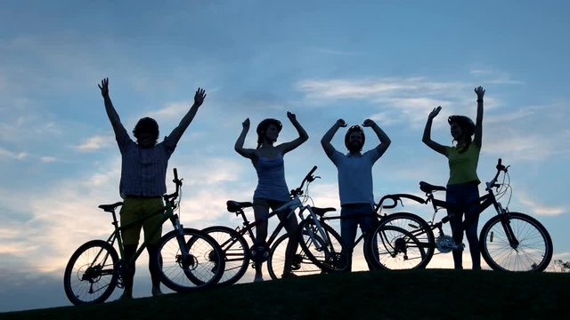 Young dancing cyclists at sunset sky. Group of young cheerful friends having rest outdoors. Happy people dancing at sunset.