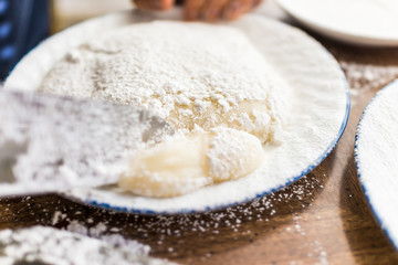 Kitchen knife cutting piece of mochi sticky glutinous rice cake dusted with starch flour to make dessert