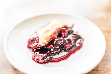 Closeup of hot fresh red cherry cobbler slice piece on white plate on table golden crust, gooey thick filling