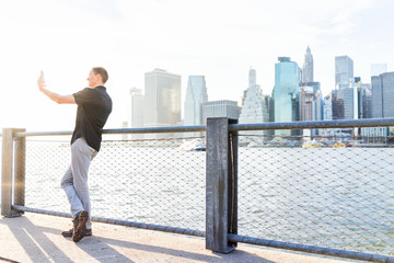 Back of young man outside outdoors in NYC New York City Brooklyn Bridge Park by east river, railing, looking at view of cityscape skyline
