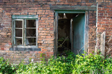 Fototapeta na wymiar An old derelict, rotted green window and door frame against a red brick wall, with overgrown plants and brambles.