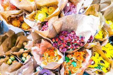 Many different types of flower bouquets in florist store shop grocery market wrapped in brown paper bags, roses, sunflowers, orange