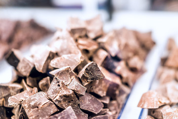 Pile of many milk dark brown chocolate pieces macro closeup chunks on tray glass display in candy shop store chocolatier