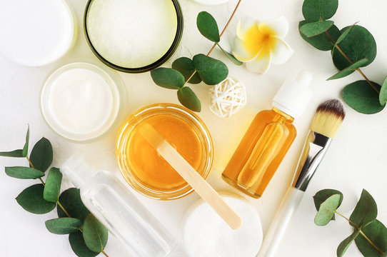 Natural cosmetics ingredients for skincare, body and hair care. Golden honey in jar and green herbal eucalyptus leaves. Top view bottles with facial treatment product white background.