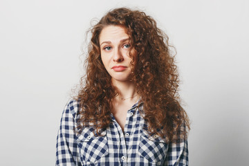 Unhappy beautiful woman with displeased look has attractive look and curly hair, looks at camera with bewilderment, being puzzled as makes serious decision, isolated over white studio background
