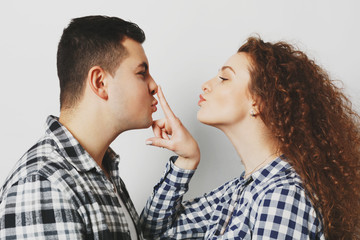 Horizontal shot of beautiful female with curly hair enjoys spending time with her boyfriend, touches his nose gently, have devoted feelings, feel love and support, poses against studio background