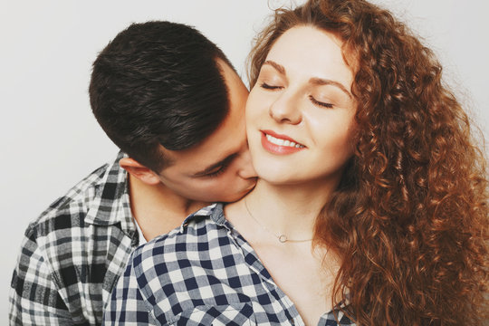 Pleased female keeps eyes shut as recieves passionate kiss in neck from her boyfriend. Young man kisses his young wife, demostrates love. Couple in love have good feelings, being very romantic