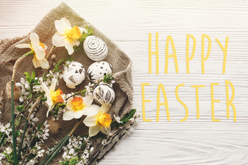happy easter text. season's greetings card. stylish easter flat lay with painted egg at rustic wooden background with spring flowers daffodils. modern top view