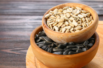 Black peeled and unpeeled sunflower seeds in a wooden bowl on a wooden table.