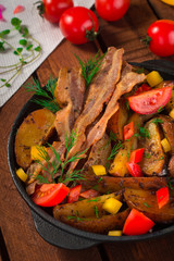 Fried potatoes with bacon and fresh tomatoes in the frying pan. Wooden rustic background. Top view
