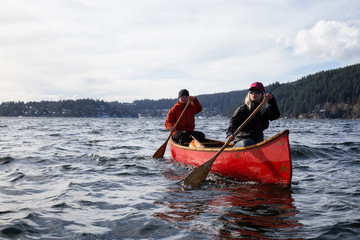 Obraz premium Couple friends on a wooden canoe are paddling in an inlet surrounded by Canadian mountains. Taken in Indian Arm, near Deep Cove, North Vancouver, British Columbia, Canada.
