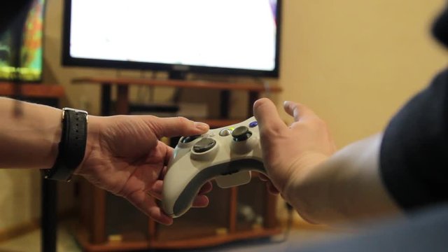 Closeup of young man hands playing video games on gaming console in front of TV widescreen