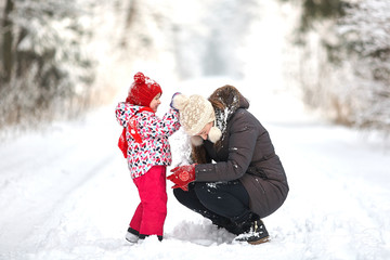Young beautiful girl whith wihite hat  posing against a winter park background and playing with the girl child with the snow in forest © Mindaugas