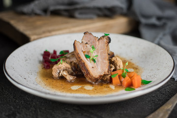 Pork ribs with beets, carrots, fried mushrooms and sauce on a white plate. Restaurant serving. Old black rustic background. Top view
