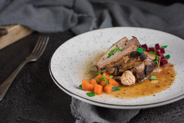 Pork ribs with beets, carrots, fried mushrooms and sauce on a white plate. Restaurant serving. Old black rustic background. Top view