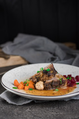 Pork ribs with beets, carrots, fried mushrooms and sauce on a white plate. Restaurant serving. Old black rustic background. Top view