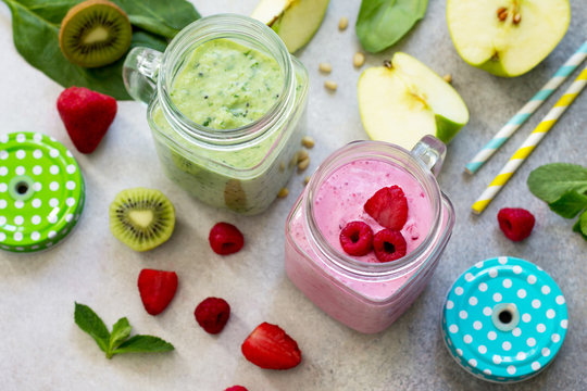 Mason jar mugs with fresh berry cocktails and green smoothies, ingredients for cooking smoothies against a background of gray stone or slate. Healthy vegan food concept.