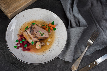 Pork ribs with beets, carrots, fried mushrooms and sauce on a white plate. Restaurant serving. Old black rustic background. Top view
