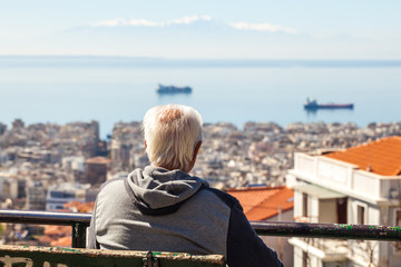 Fototapeta na wymiar Old man sitting on a bench looking at the gulf in Thessaloniki, Greece