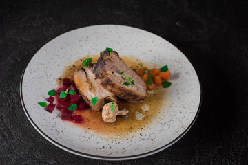 Pork ribs with beets, carrots, fried mushrooms and sauce on a white plate. Restaurant serving. Old black rustic background. Top view