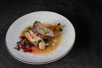 Pork ribs with beets, carrots, fried mushrooms and sauce on a white plate. Restaurant serving. Old black rustic background. Top view