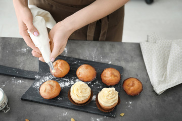 Woman decorating tasty cupcakes with cream at table