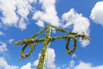 Maypole made of green leaf and the blue sky and some white clouds behind